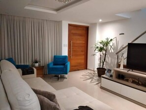 Ein modernes Wohnzimmer mit einer Couch, einem blauen Sessel, einem Fernseher, einer Topfpflanze und einer Holztür.
