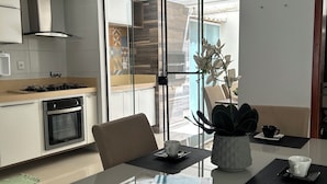 Une cuisine moderne équipée d’une cuisinière à gaz, d’un four et d’un coin repas avec une table en verre, des chaises et une plante en pot.