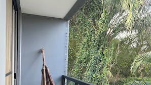 Un hamac sur un balcon donnant sur un feuillage dense.