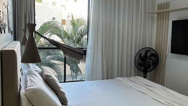 Une chambre d’hôtel avec un lit, une télévision, un ventilateur et un balcon donnant sur des palmiers.