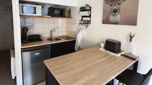 Cocina compacta con microondas, tostadora y lavabo. Hay un reloj en la pared y un cuadro de un ciervo sobre la encimera.