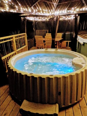 A hot tub surrounded by wooden chairs and a railing, with string lights overhead.