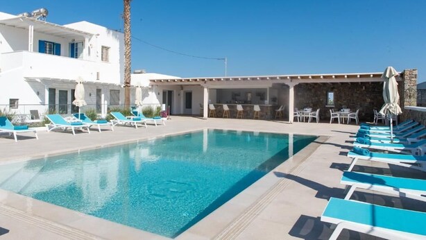A swimming pool with lounge chairs, a covered area, and a building with a stone facade. - Diogenis Village Mykonos (Mykonos)