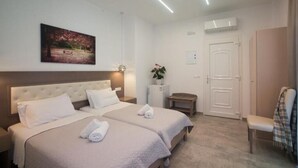 A hotel room with two beds, a bench, a door, and a painting on the wall. - Diogenis Village Mykonos (Mykonos)