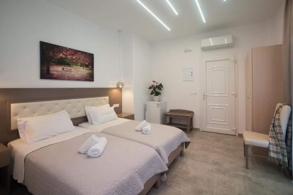 Une chambre d’hôtel avec deux lits, un banc, une porte et un tableau au mur.