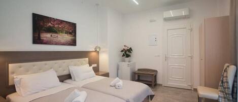 A hotel room with two beds, a bench, a door, and a painting on the wall.