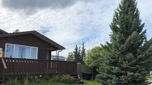 A residential house with a deck, a wooden fence, and a large evergreen tree.