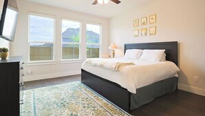 A bedroom with a bed, a ceiling fan, a TV, and a window with a view of mountains.