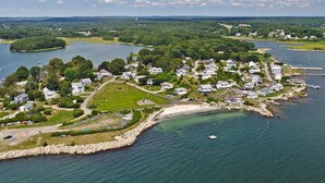 An aerial view of a coastal area with a marina, houses, and a small island with a grassy area and a flag. - Awesome Oceanfront 4-bedroom watersports cottage in Mystic (Stonington)