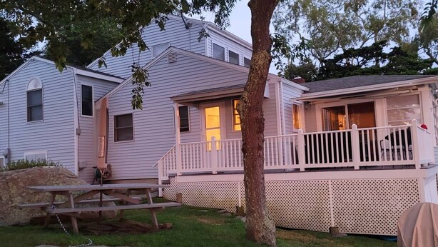 A two-story house with a porch, a picnic table, and a large tree in the foreground. - Awesome Oceanfront 4-bedroom watersports cottage in Mystic (Stonington)