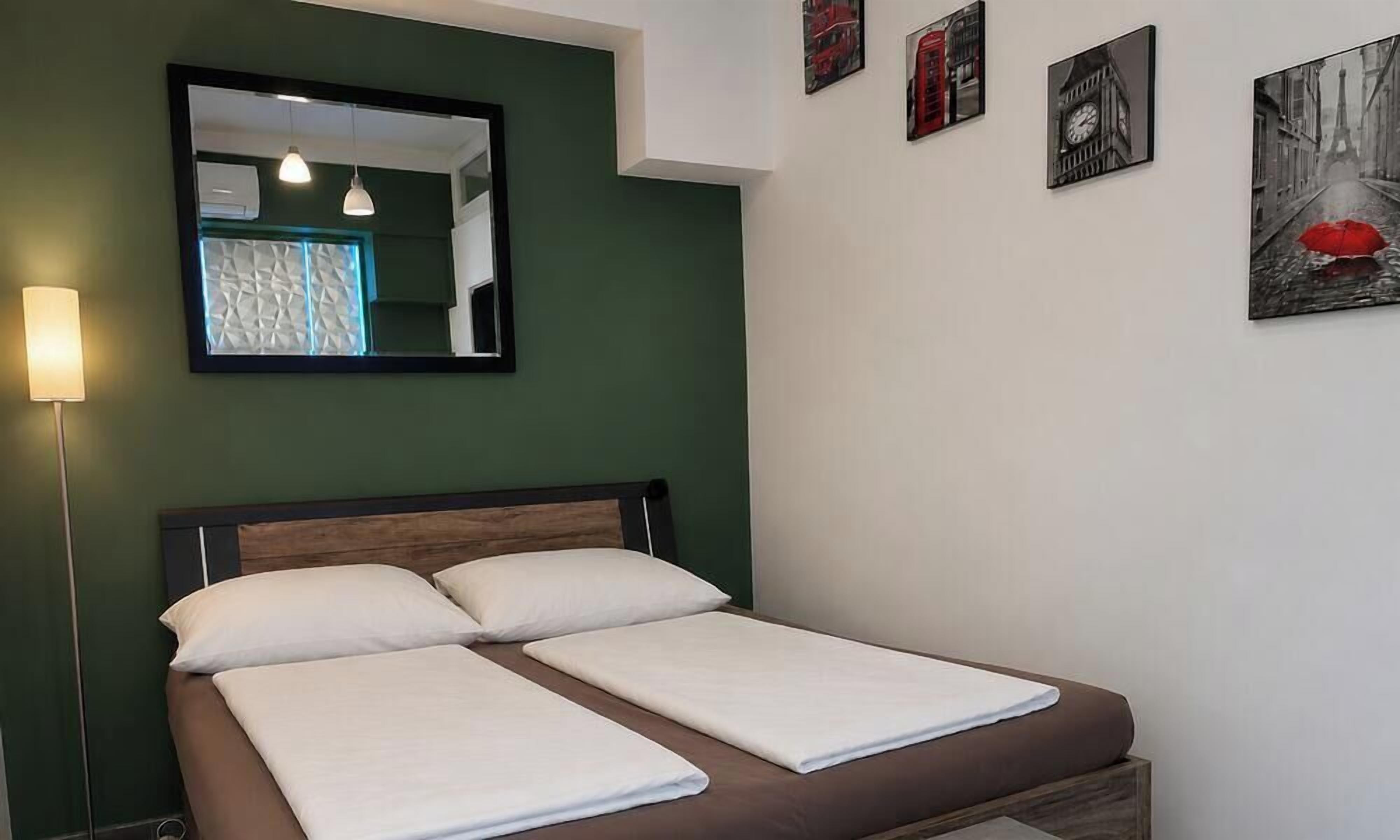 A single bed with a wooden headboard, a bedside lamp, and a mirror above it.