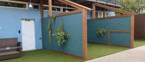 Un edificio moderno con fachada azul, una terraza de madera y un césped artificial verde.