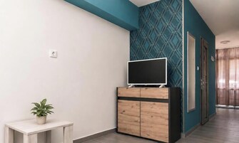 Habitación con televisión de pantalla plana sobre un mueble de madera, una planta en maceta sobre una mesita y un papel tapiz estampado.