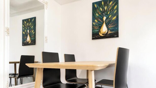 A conference room with a wooden table and black chairs, two paintings on the wall, and a mirror reflecting the room. - Tisza Gyöngye Apartmanok (Szeged)