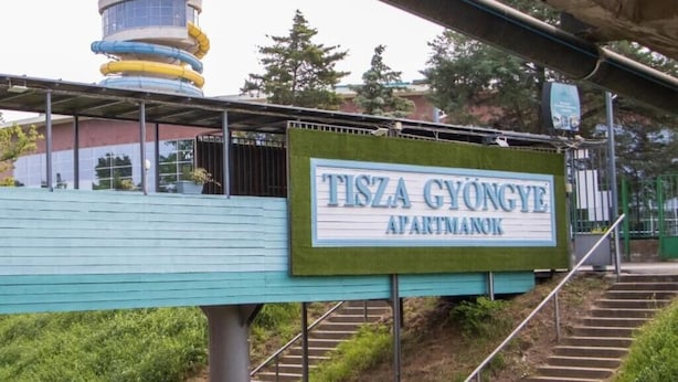 Une enseigne indiquant « TISZA GYONGYE APARTMANOK », avec un escalier menant à celle-ci.