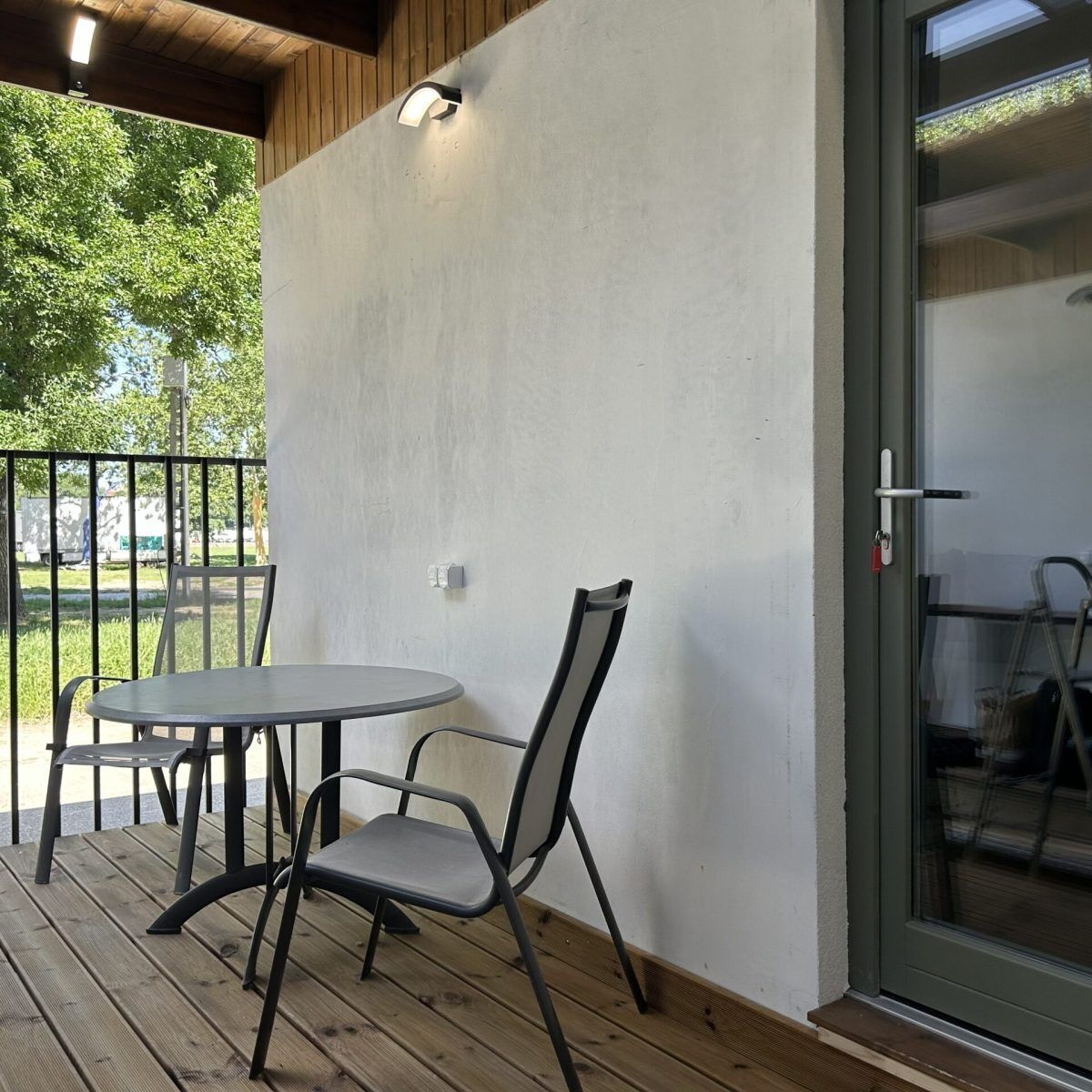 Een terras met een tafel en stoelen, een houten terras en een glazen deur die leidt naar een binnenruimte.