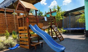 A wooden play structure with a slide, a swing set, and a climbing ladder. - Tisza Gyöngye Apartmanok (Szeged)