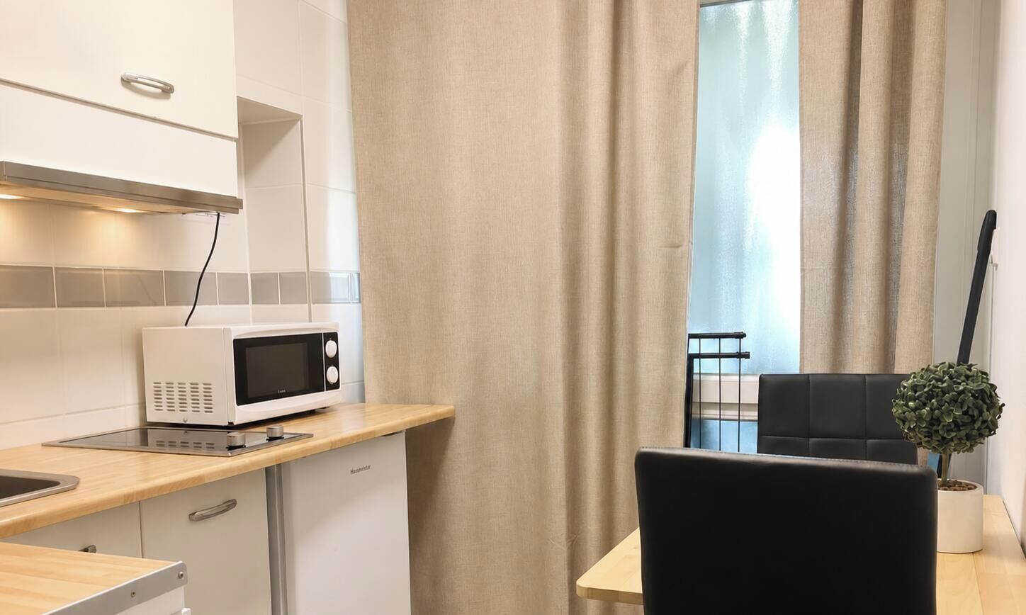 A kitchenette with a microwave, a small refrigerator, a wooden countertop, and a black chair.