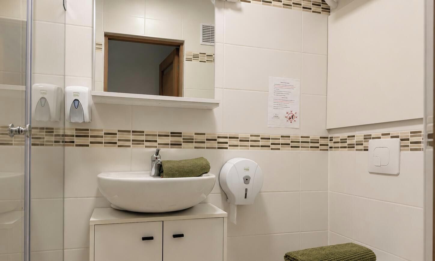 Ein Badezimmer mit Waschbecken, Spiegel, Handtuchspender und einem kleinen Handtuch auf der Ablagefläche.