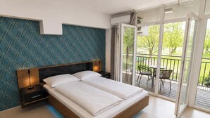 A modern bedroom with a large bed, a nightstand, and a view of a balcony with outdoor furniture. - Tisza Gyöngye Apartmanok (Szeged)
