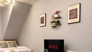A dining area with a table set for two, a television displaying 'NETFLIX,' and a cozy seating area with a sofa and decorative pillows.