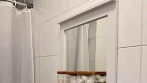 A bathroom with a white tiled wall, a wooden shelf with toiletries, and a shower curtain.