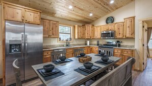 A modern kitchen with wooden cabinets, stainless steel appliances, and a large dining table. - Secluded Mountain Cabin with Hot Tub & Fire pit on 4 acres (Murphy)