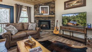 Ein gemütliches Wohnzimmer mit Kamin, Ledersofa, Couchtisch aus Holz und Fernseher.