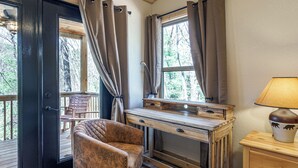 A room with a wooden desk, a leather chair, a lamp, and a view of trees through the windows. - Secluded Mountain Cabin with Hot Tub & Fire pit on 4 acres (Murphy)