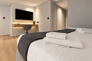 Una habitación de hotel moderna con una cama grande, un televisor de pantalla plana en la pared y una mesita de noche con lámpara.