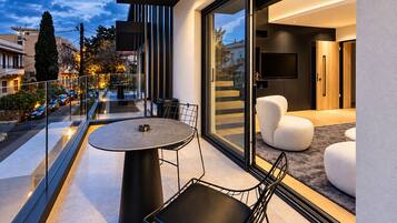 Un balcón moderno con puerta de cristal que da a un espacio interior, una mesa redonda con sillas y vista a la calle.