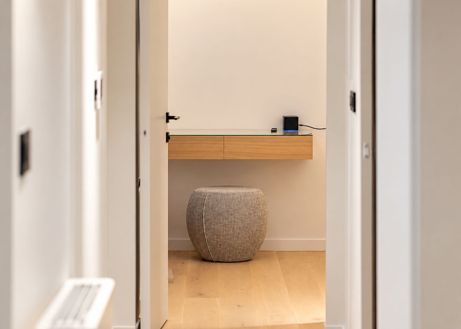 Un pasillo que conduce a un baño con tocador de madera y un taburete redondo.