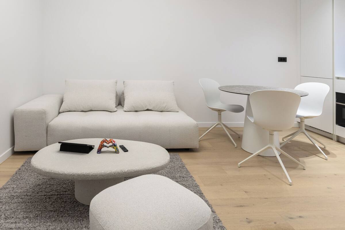 A modern living room with a sofa, round coffee table, ottoman, and a dining area with chairs.