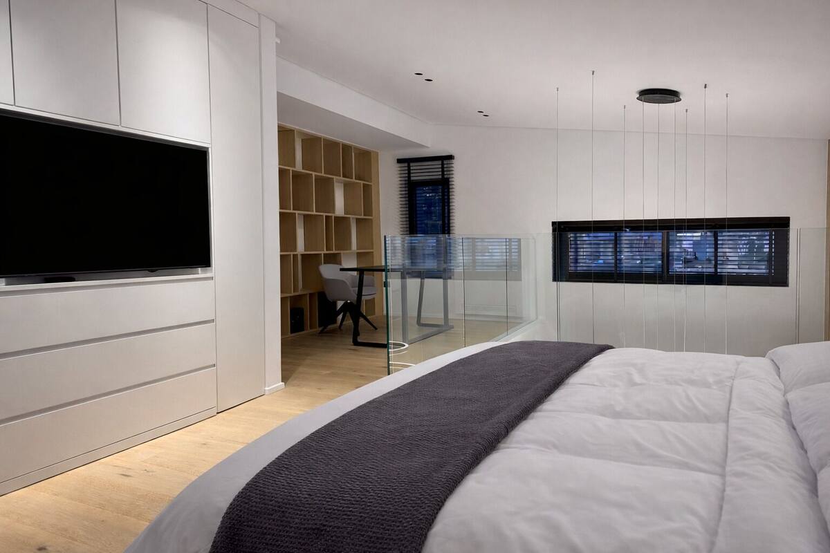 A bedroom with a bed, a TV, a desk, and a shelving unit.
