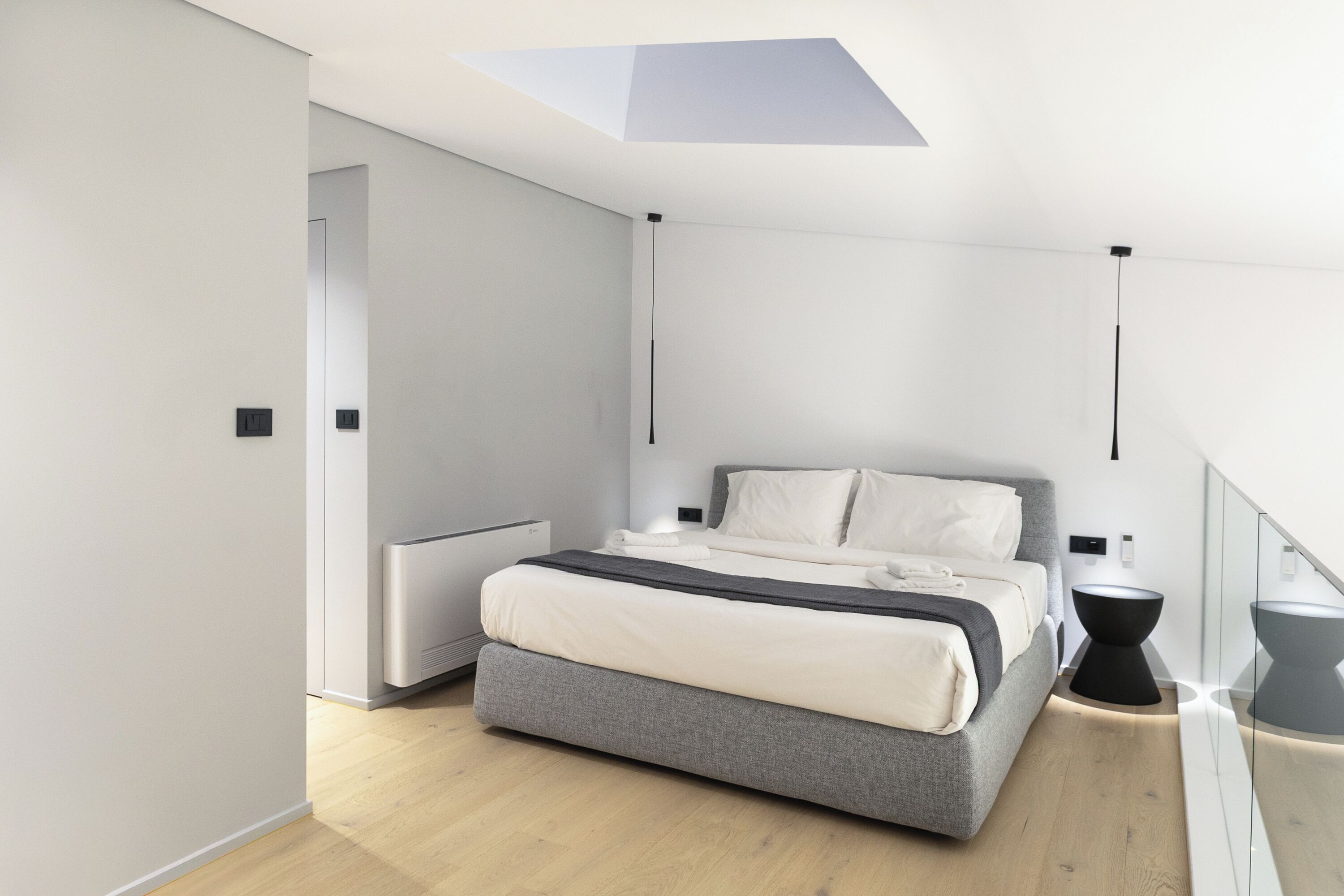 A modern bedroom with a bed, bedside tables, a radiator, and a skylight.