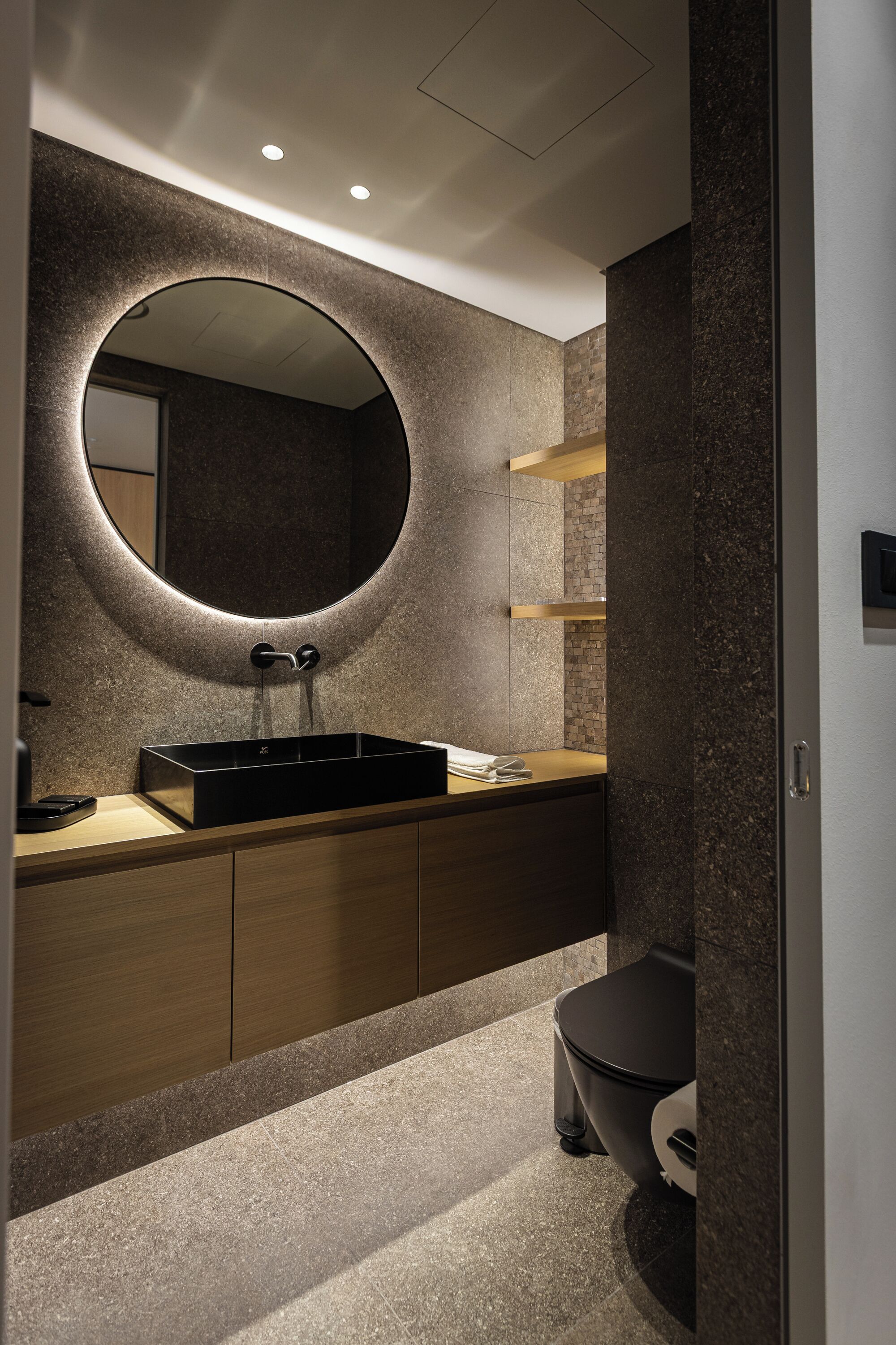 A modern bathroom with a round mirror, a black sink, and a toilet.