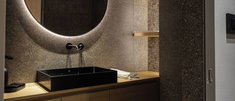 A modern bathroom with a round mirror, a black sink, and a toilet.