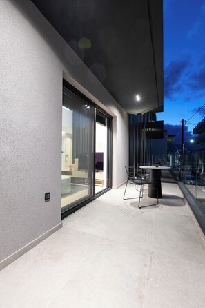 A modern outdoor patio with a glass door leading to a room, a round table, and a chair. - KALVOKORESI 16 I PREMIUM APARTMENTS (Chios)
