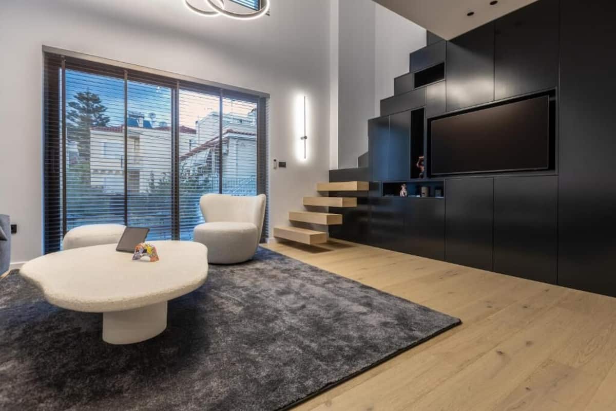 A modern living room with a large TV, a white sofa, a round coffee table, and a staircase leading to an upper level.