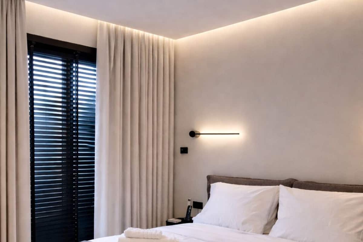 A modern hotel room with a large bed, a bedside table, a nightstand, and a window with curtains.