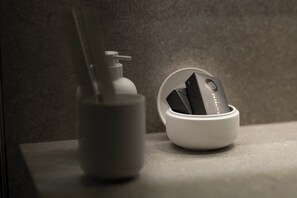 A bathroom with a white soap dispenser and a white bowl with a black object inside. - KALVOKORESI 16 I PREMIUM APARTMENTS (Chios)