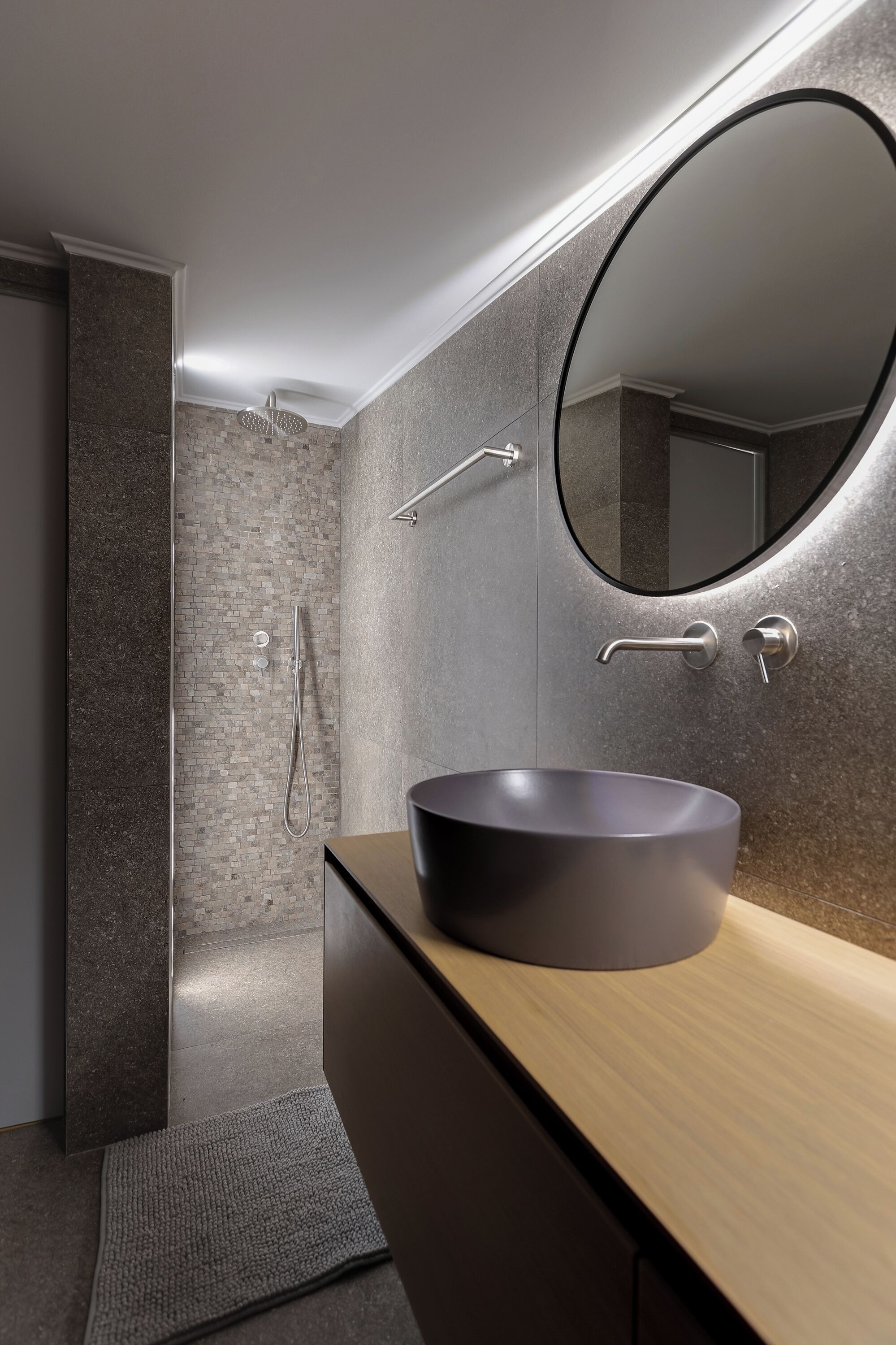 Une salle de bain moderne avec un grand miroir, un lavabo rond et un espace douche.