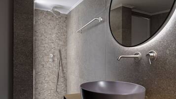 A modern bathroom with a large mirror, a round sink, and a shower area.