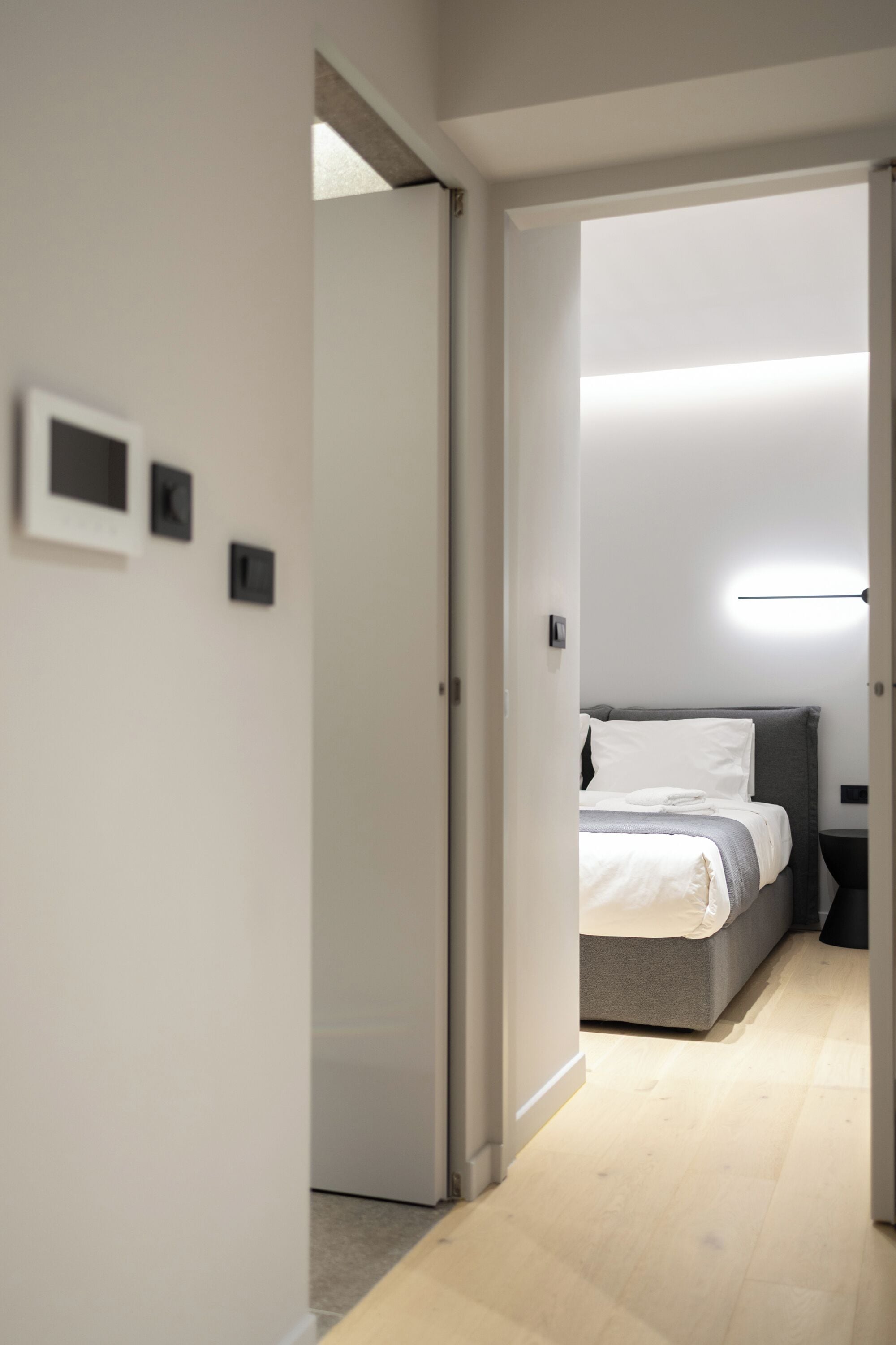 A modern hotel room with a bed, bedside table, and a wall-mounted light fixture.