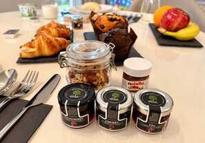 A breakfast setting with croissants, muffins, a jar of nuts, and jars of fruit jam. - KALVOKORESI 16 I PREMIUM APARTMENTS (Chios)