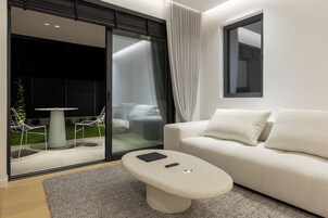 Una sala de estar moderna con un sofá, una mesa de centro y un ventanal de vidrio que da a un espacio exterior con sillas y una mesa.