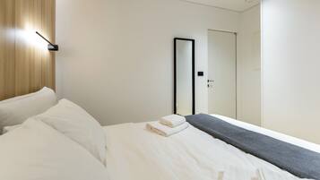 Quarto de hotel com uma cama, abajur, espelho e porta.
