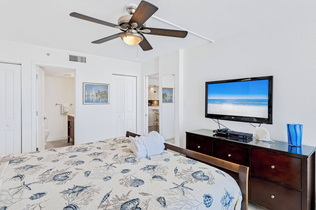 Een slaapkamer met een bed, een plafondventilator, een televisie en een dressoir.