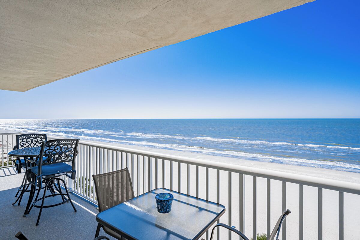 Ein Balkon mit Blick auf das Meer, mit Metallstühlen, einem Tisch und einem blauen Glas.