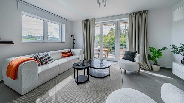 Un salon moderne avec un canapé, une table basse et un fauteuil, de grandes fenêtres et un balcon.
